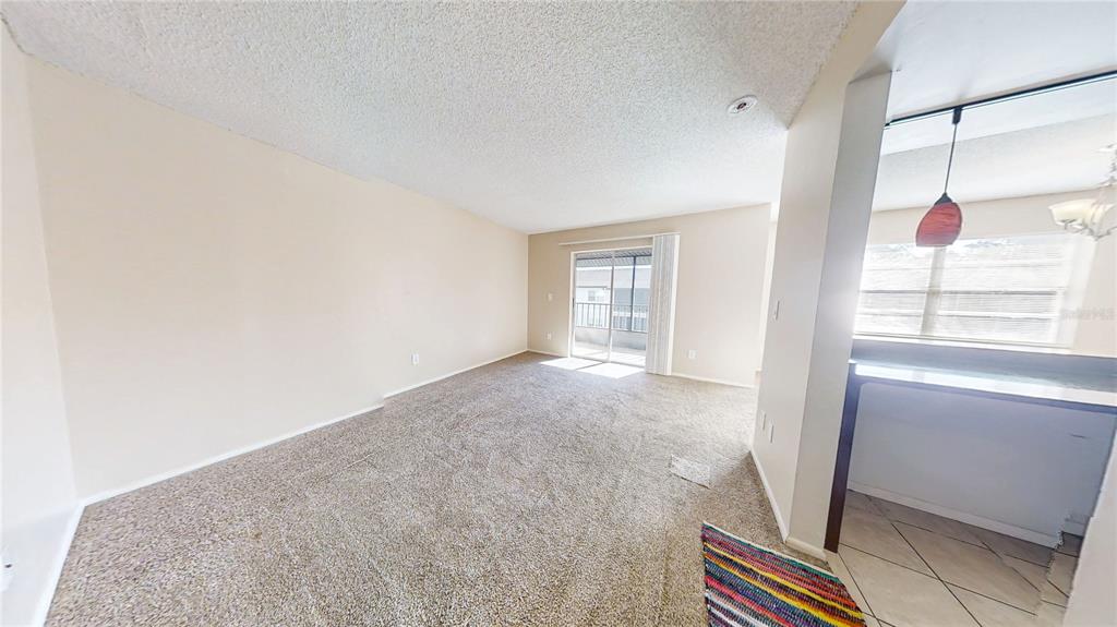 An empty living room with beige carpet, light walls, and a sliding glass balcony door — 417 BANANA CAY DRIVE UNIT J, SOUTH DAYTONA, FL