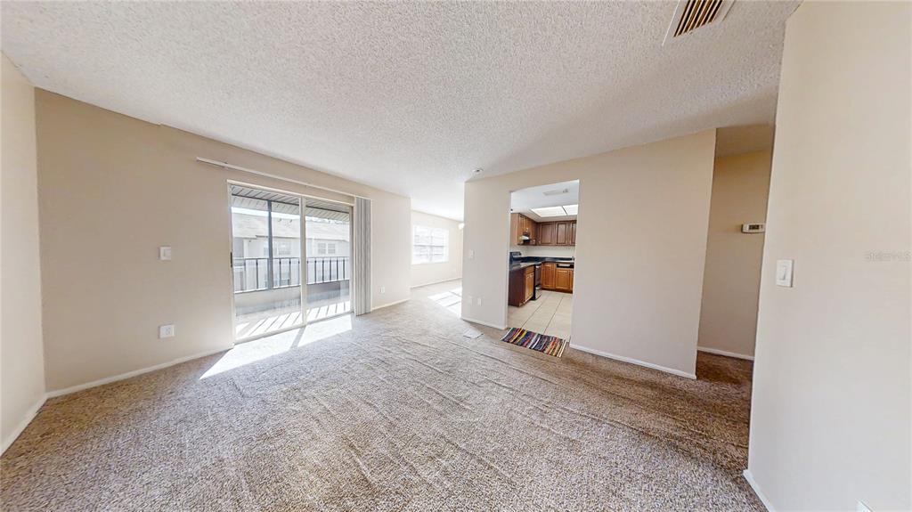 A carpeted living room with a sliding glass door leads to a kitchen with cabinets — 417 BANANA CAY DRIVE UNIT J, SOUTH DAYTONA, FL