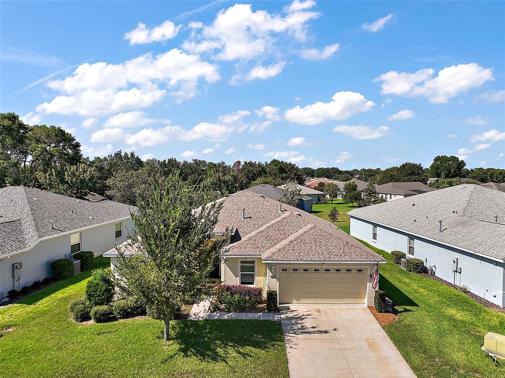 An aerial view of a single-story suburban house with a tan garage and shingled roof — 27102 CAMERONS RUN, LEESBURG, FL