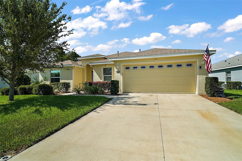 A single-story house with a yellow stucco exterior, a two-car garage, and a concrete driveway — 27102 CAMERONS RUN, LEESBURG, FL