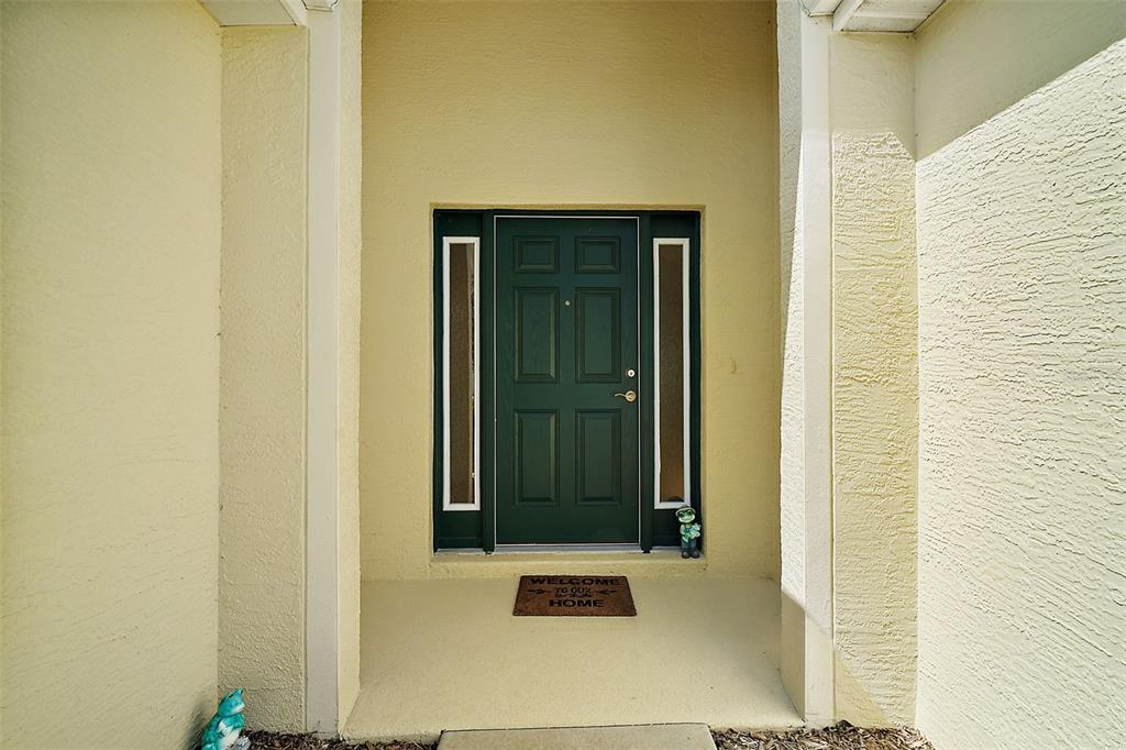 A dark green front door with sidelights is centered in a covered entryway — 27102 CAMERONS RUN, LEESBURG, FL