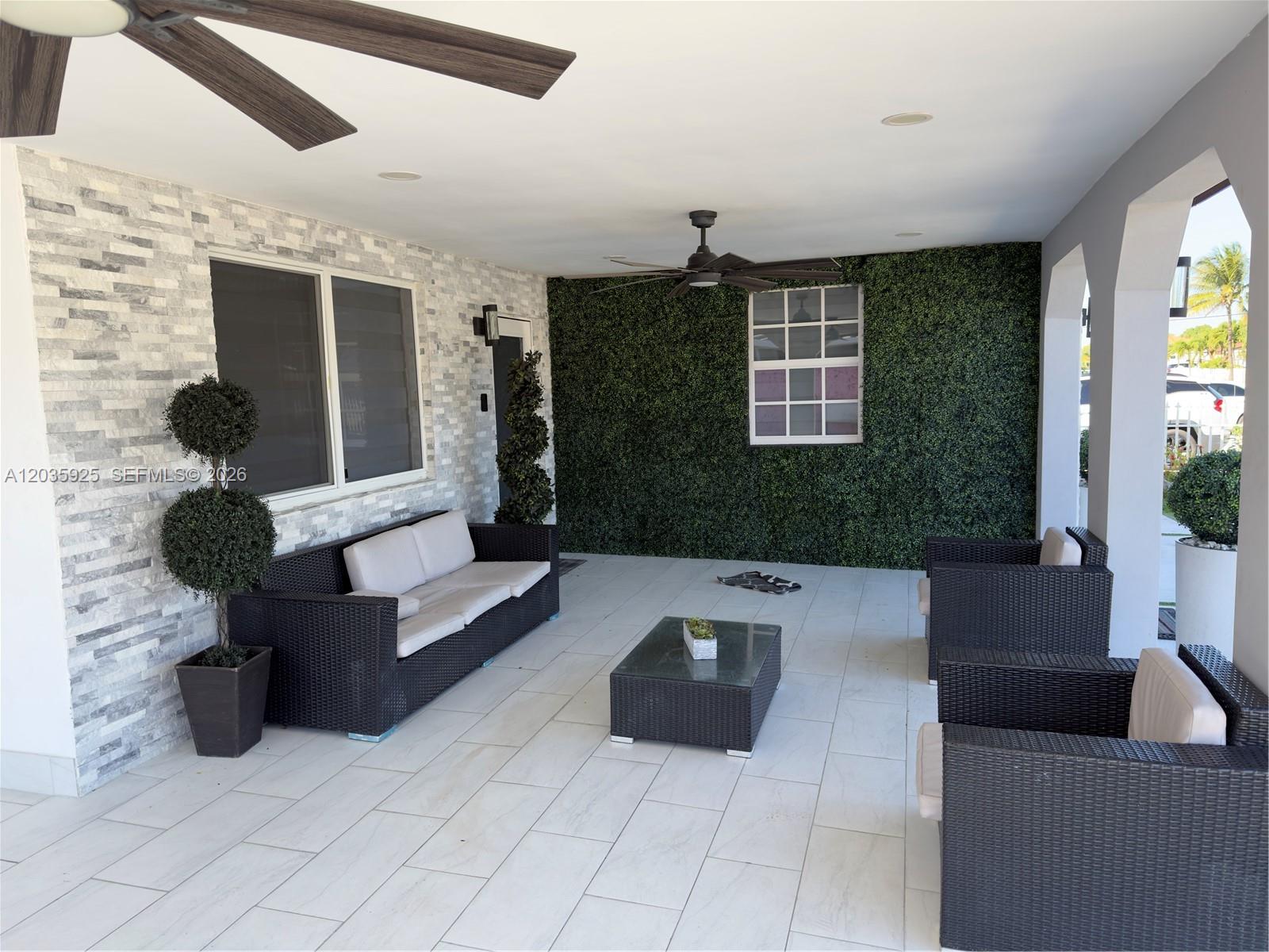 A covered patio features a stone accent wall, a green hedge wall, and wicker furniture — 224 E 42nd St, Hialeah FL 33013, HIALEAH, FL