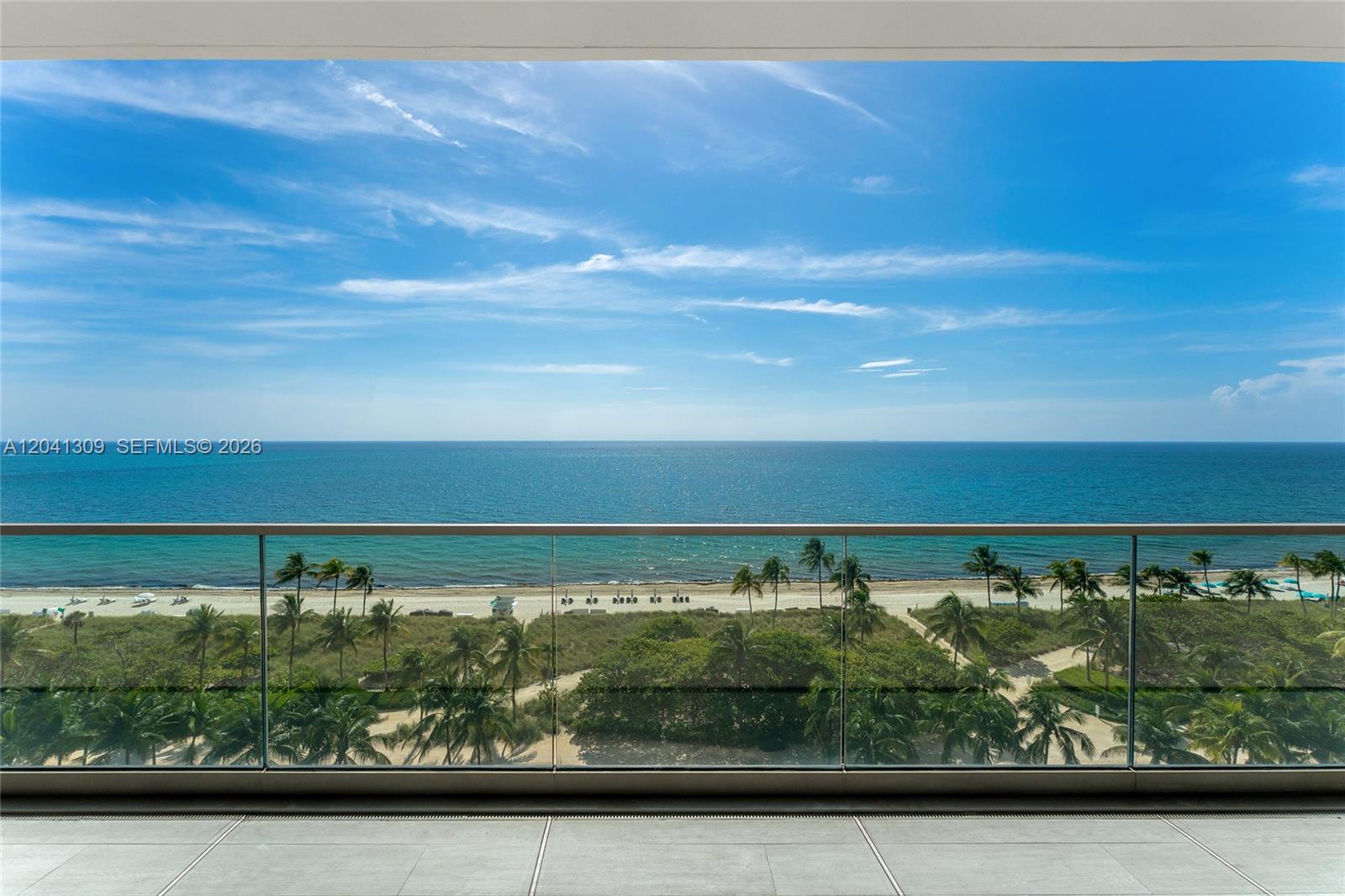 A balcony with a glass railing overlooks a sandy beach, palm trees, and the ocean — 10201 Collins Ave # 906, Bal Harbour FL 33154, BAL HARBOUR, FL