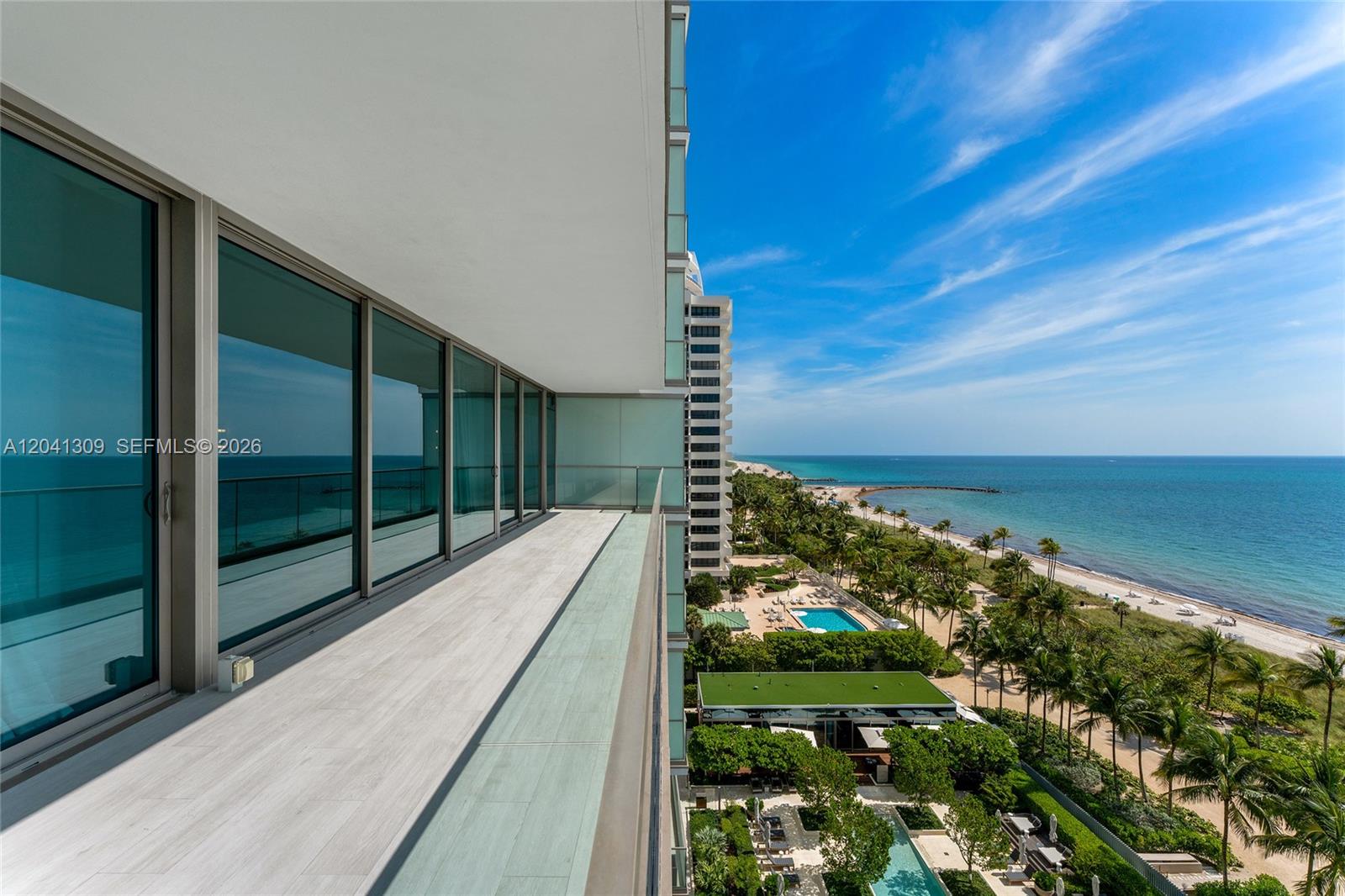 A high-rise balcony with light-colored flooring overlooks a beach, ocean, and swimming pool area — 10201 Collins Ave # 906, Bal Harbour FL 33154, BAL HARBOUR, FL