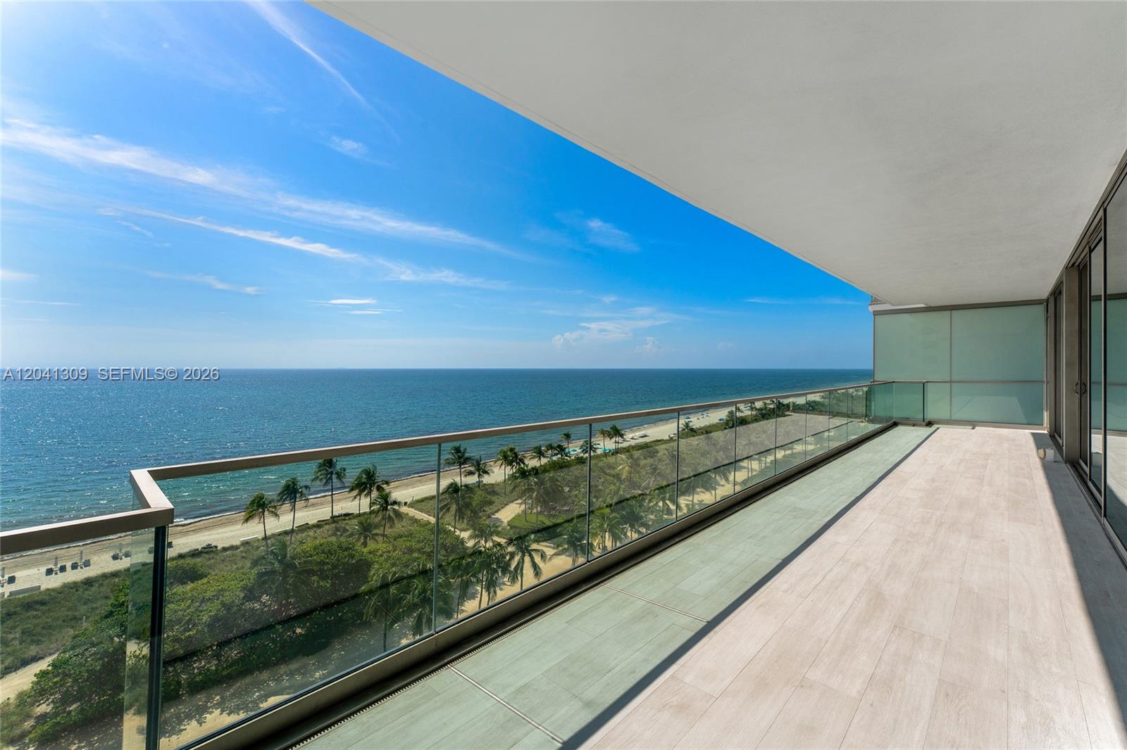 A spacious balcony features a glass railing overlooking a beach, palm trees, and the ocean — 10201 Collins Ave # 906, Bal Harbour FL 33154, BAL HARBOUR, FL