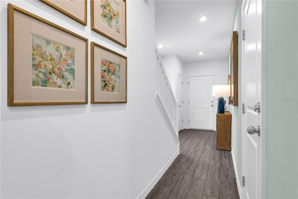 A hallway features white walls, dark wood-look flooring, a staircase, and framed artwork — 1928 FAN PALM DRIVE, DAVENPORT, FL