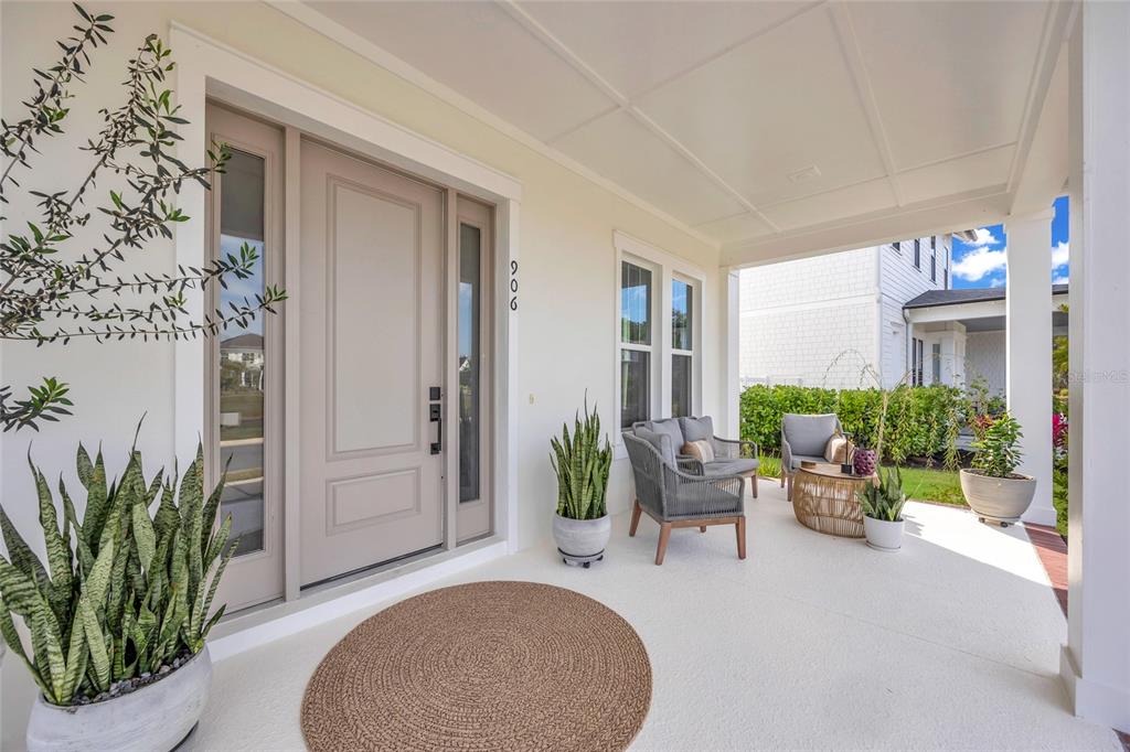 A covered front porch features a neutral door, gray wicker furniture, and potted snake plants — 906 ALLENDALE LANE, WINTER GARDEN, FL