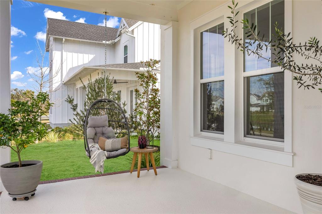 A covered porch features a hanging egg chair, a small side table, and potted plants — 906 ALLENDALE LANE, WINTER GARDEN, FL