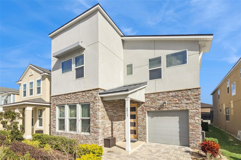 A two-story house features a stone facade, a single-car garage, and a light-colored stucco exterior — 8913 COCONUT BREEZE DRIVE, KISSIMMEE, FL