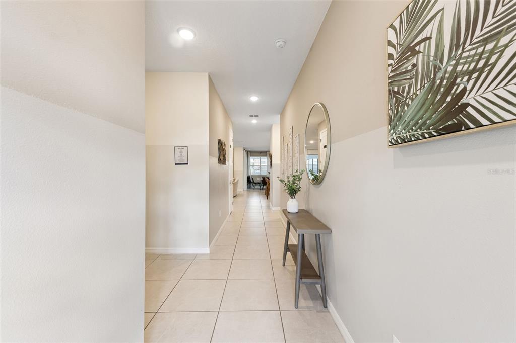 A tiled hallway features a console table, a round mirror, and wall art — 8913 COCONUT BREEZE DRIVE, KISSIMMEE, FL
