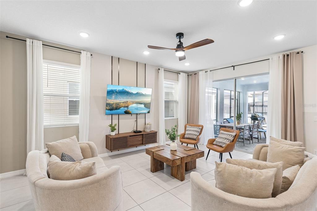 A modern living room features a wall-mounted television, wooden media console, and neutral-toned furniture — 8913 COCONUT BREEZE DRIVE, KISSIMMEE, FL