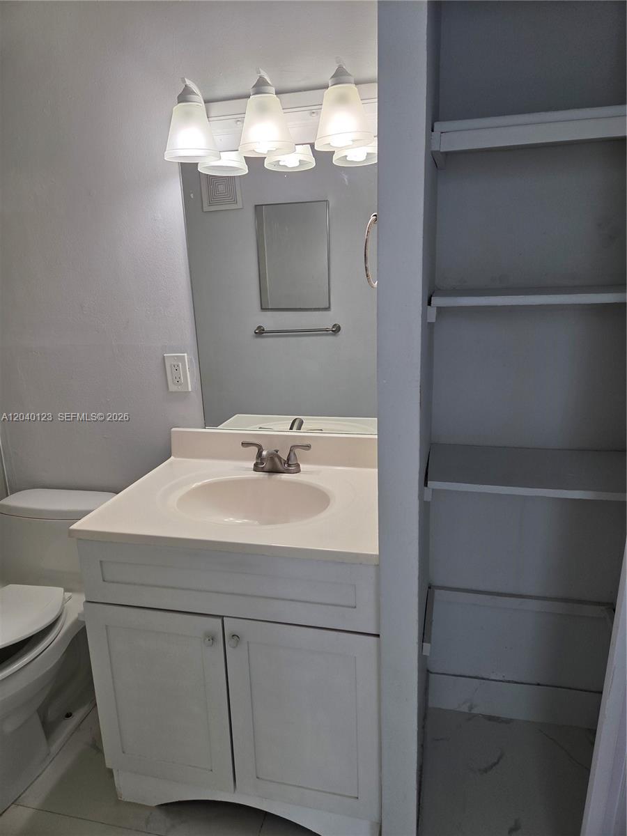 A bathroom features a white vanity with a sink, a mirror, and built-in shelving — MIAMI, FL