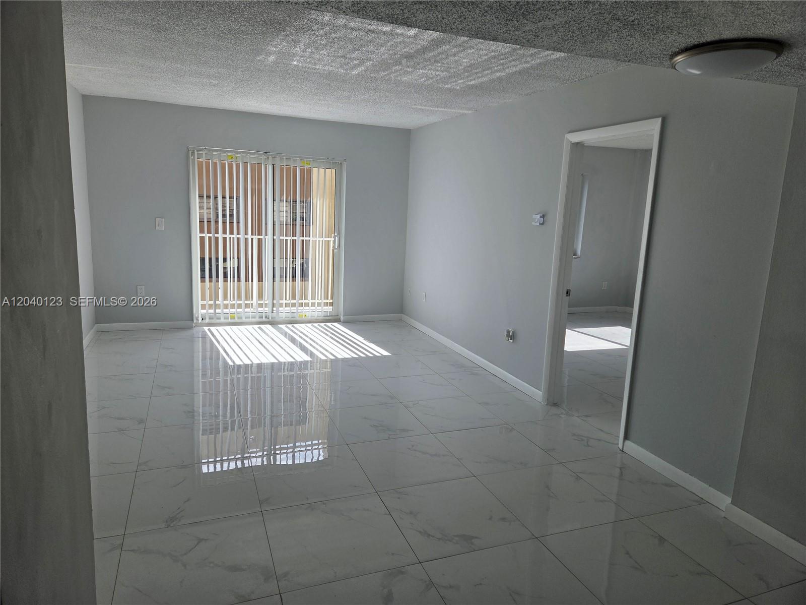 A bright living room features white marble-look tile floors and a sliding glass door — MIAMI, FL