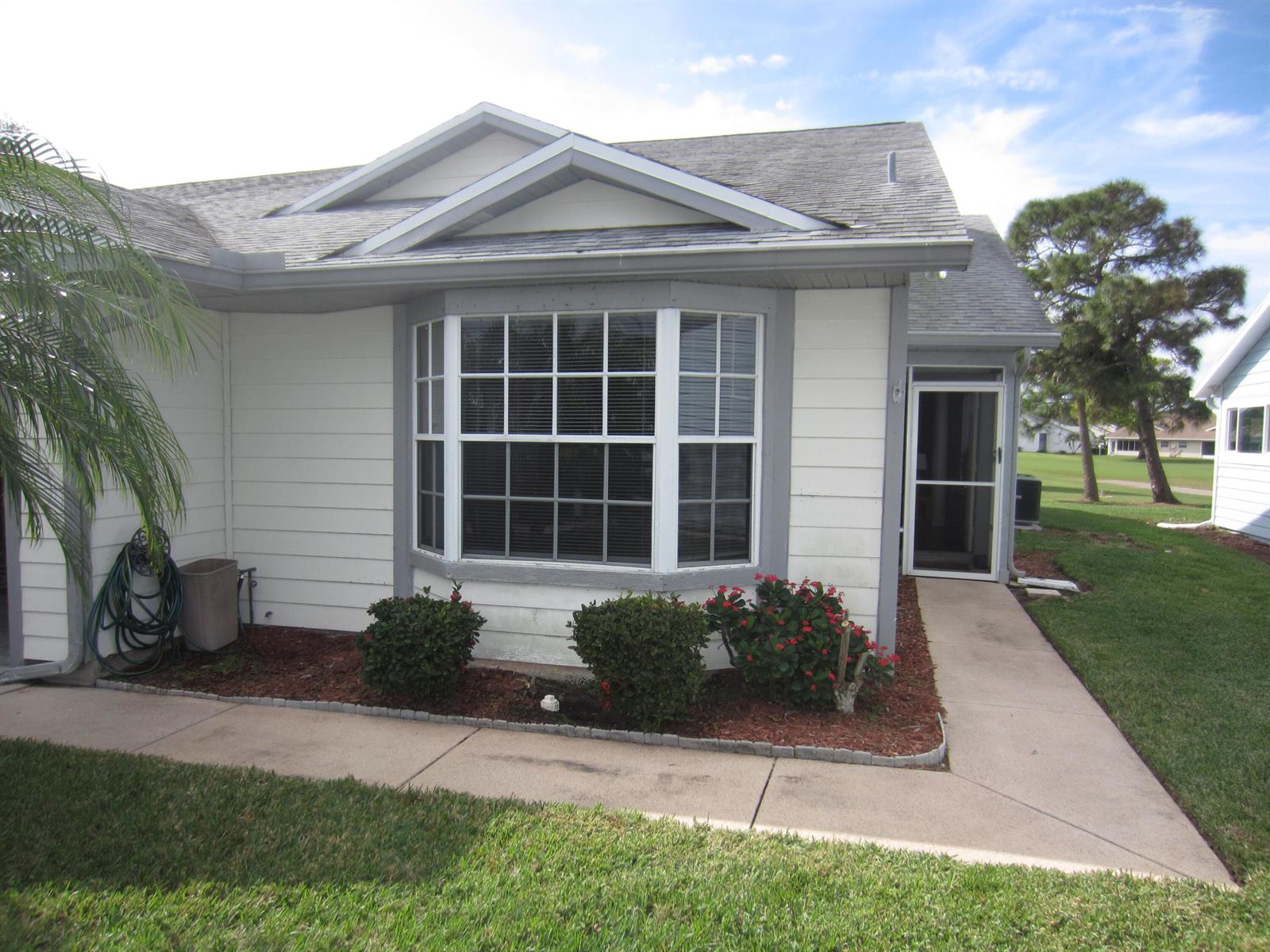 A white house exterior features a bay window, a concrete walkway, and a small garden — 4045 Gator Trace Road, Fort Pierce FL 34982, FORT PIERCE, FL