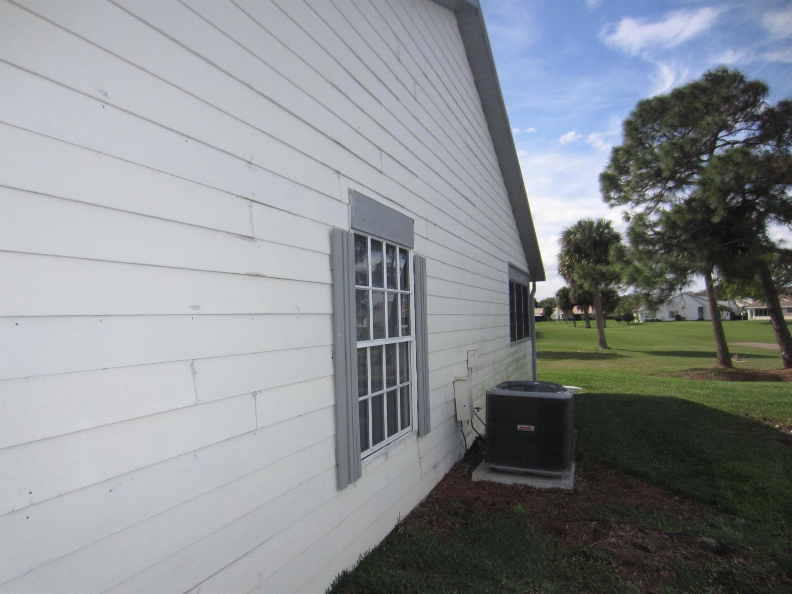 The side exterior of a white house features horizontal siding, a window, and an AC unit — 4045 Gator Trace Road, Fort Pierce FL 34982, FORT PIERCE, FL