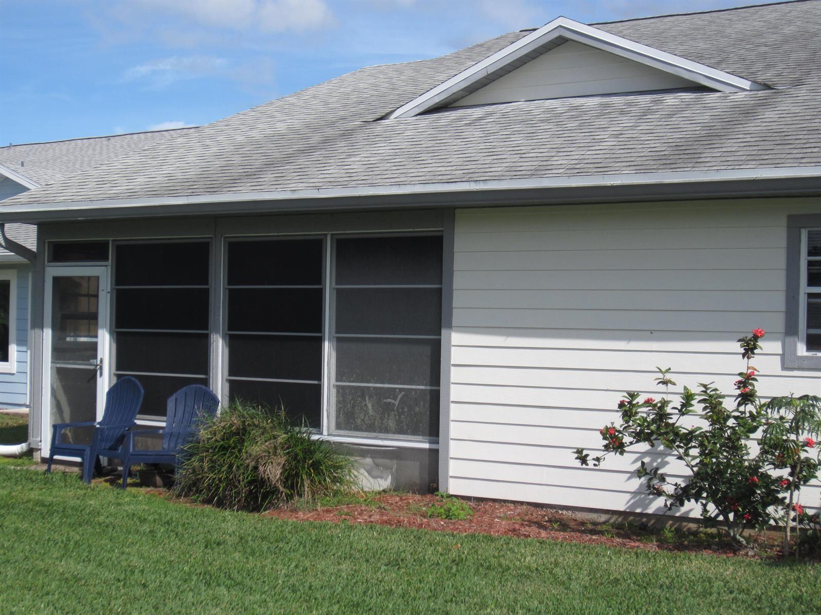 A white house exterior features a screened-in porch, blue chairs, and a flowering bush — 4045 Gator Trace Road, Fort Pierce FL 34982, FORT PIERCE, FL
