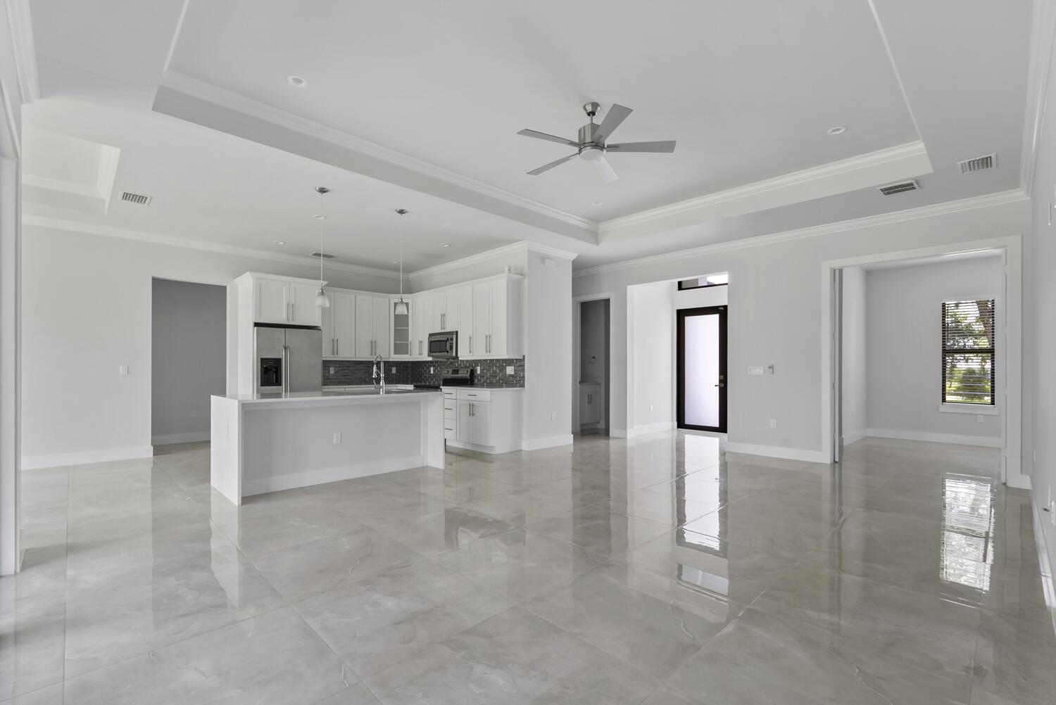 A bright, open-concept kitchen and living area features white cabinetry, gray tile flooring, and recessed lighting — 1412 22nd Avenue NE, Naples FL 34120, NAPLES, FL