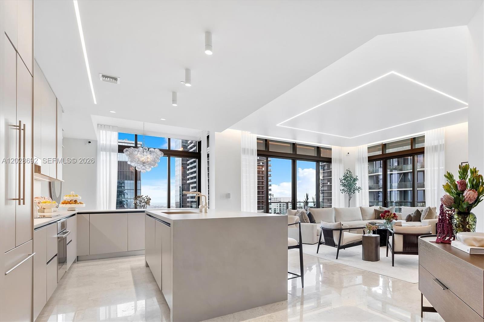 A modern open-concept kitchen and living area with light cabinetry, stone floors, and floor-to-ceiling windows — 88 SW 7th St # 4001, Miami FL 33130, MIAMI, FL