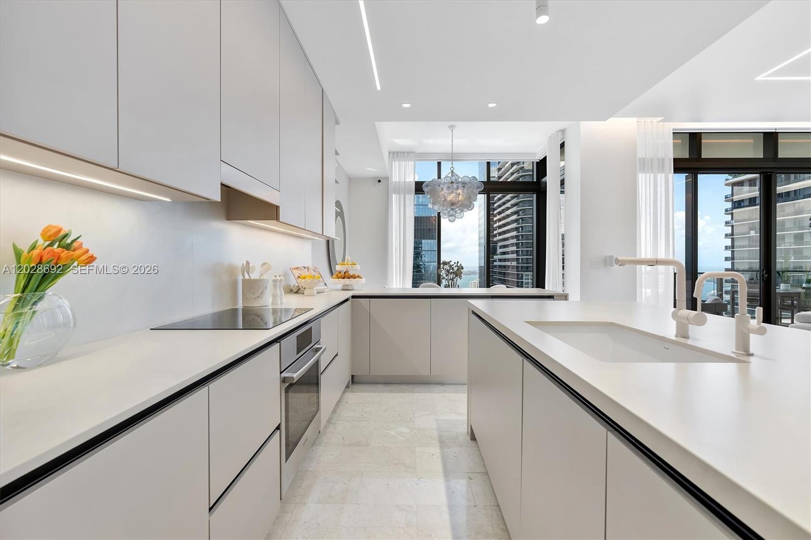 A modern white kitchen features a central island, sleek cabinetry, and floor-to-ceiling city views — 88 SW 7th St # 4001, Miami FL 33130, MIAMI, FL