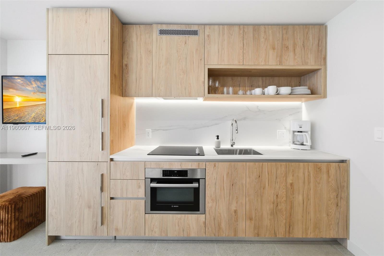 A modern kitchenette features light wood cabinetry, a marble backsplash, and stainless steel appliances — 11 NE 6th St # 1802, Miami FL 33132, MIAMI, FL