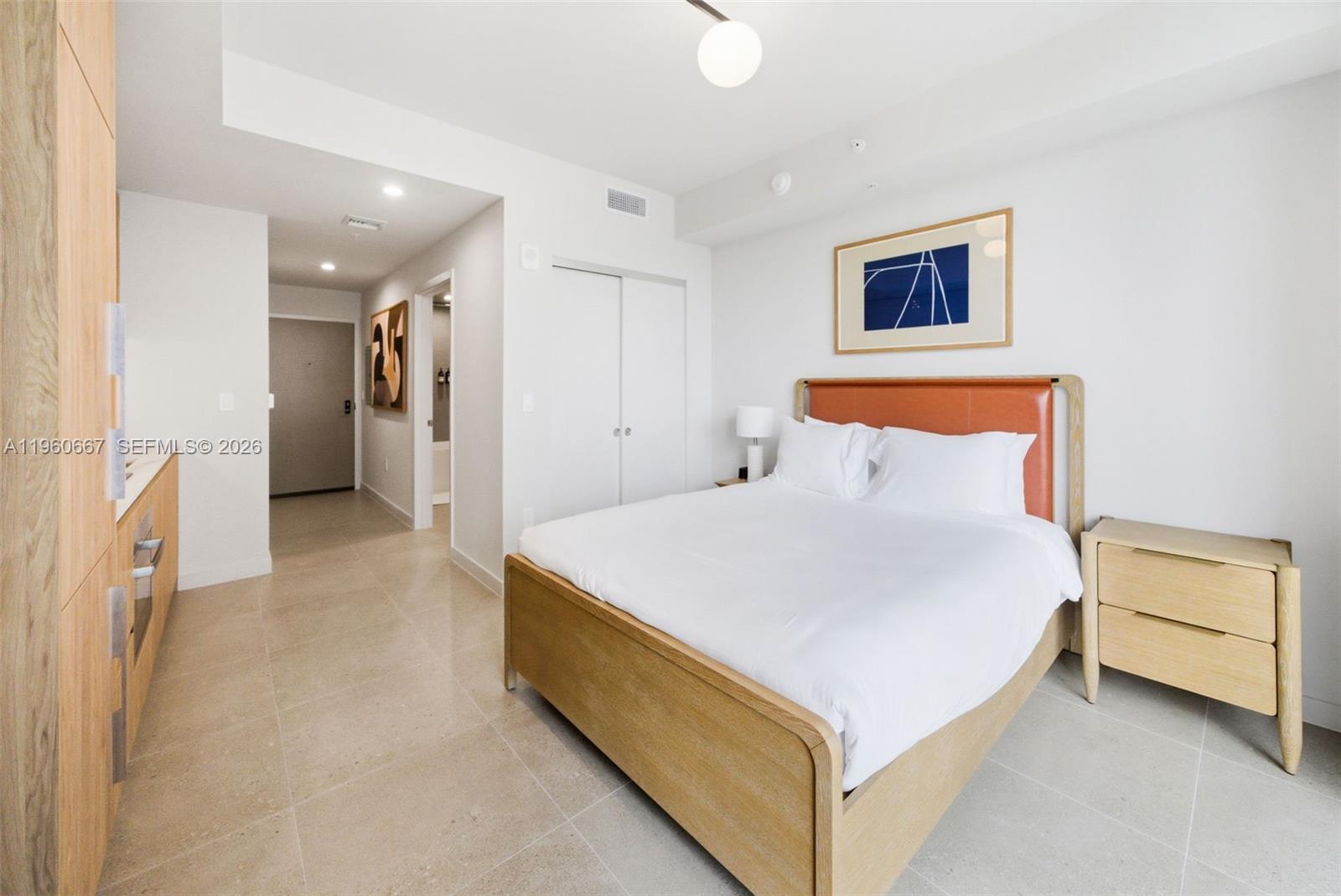 A bedroom features a wooden bed frame, light tile flooring, and a small kitchen area — 11 NE 6th St # 1802, Miami FL 33132, MIAMI, FL