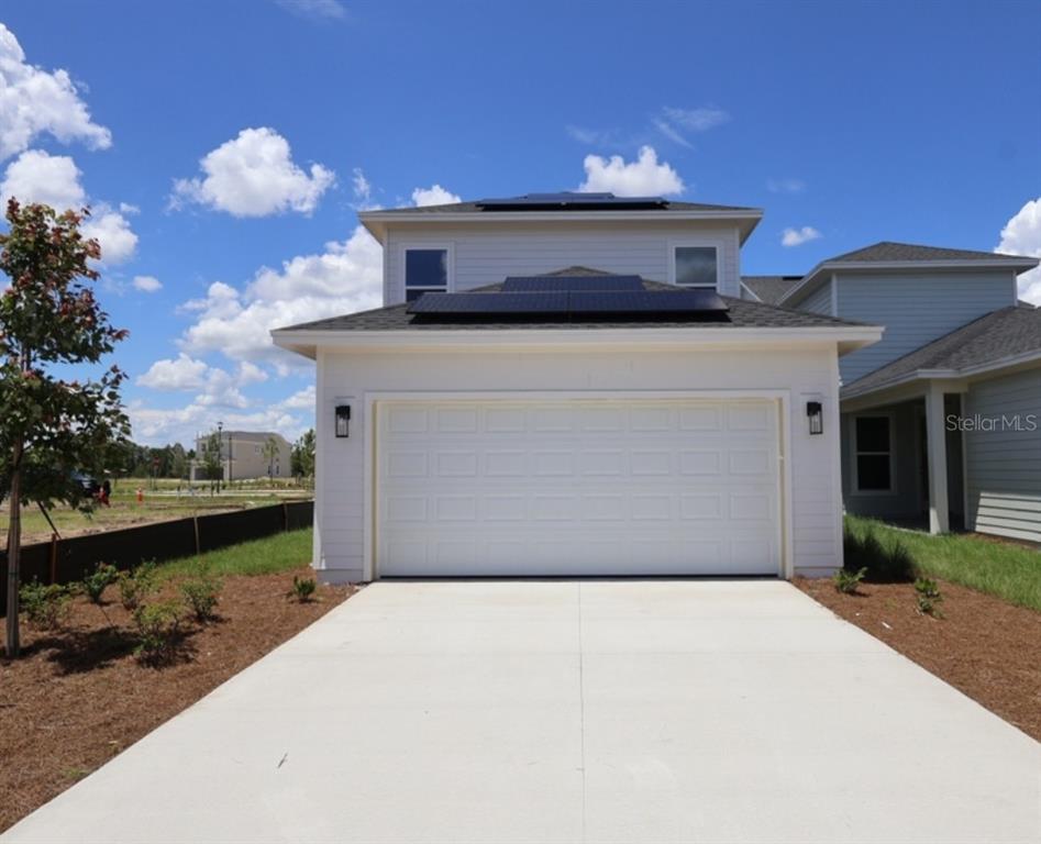 A two-story house exterior features a white garage, solar panels on the roof, and landscaping — 3211 VOYAGER AVENUE, ST CLOUD, FL