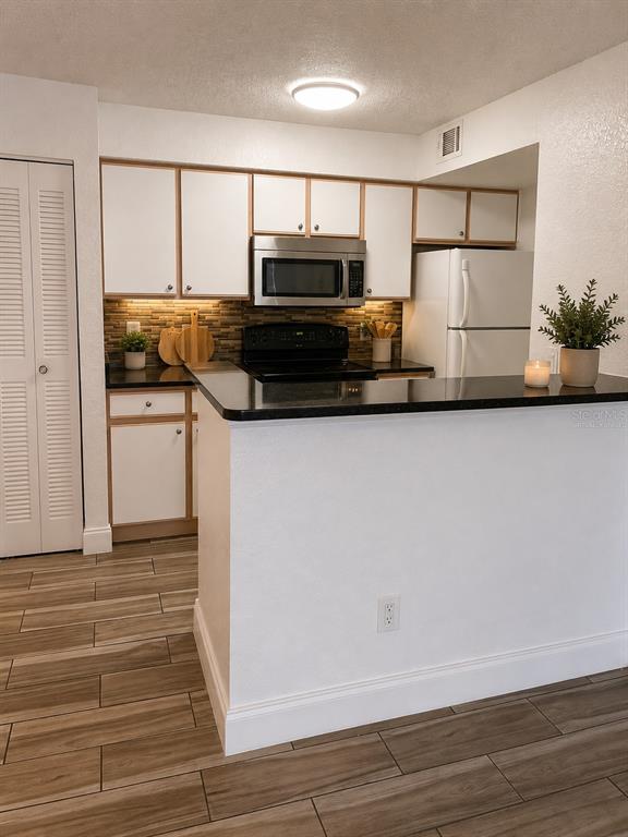 A kitchen features white cabinets, a black countertop, stainless steel appliances, and wood-look tile flooring — 2208 ANTIGUA PLACE UNIT 938, KISSIMMEE, FL