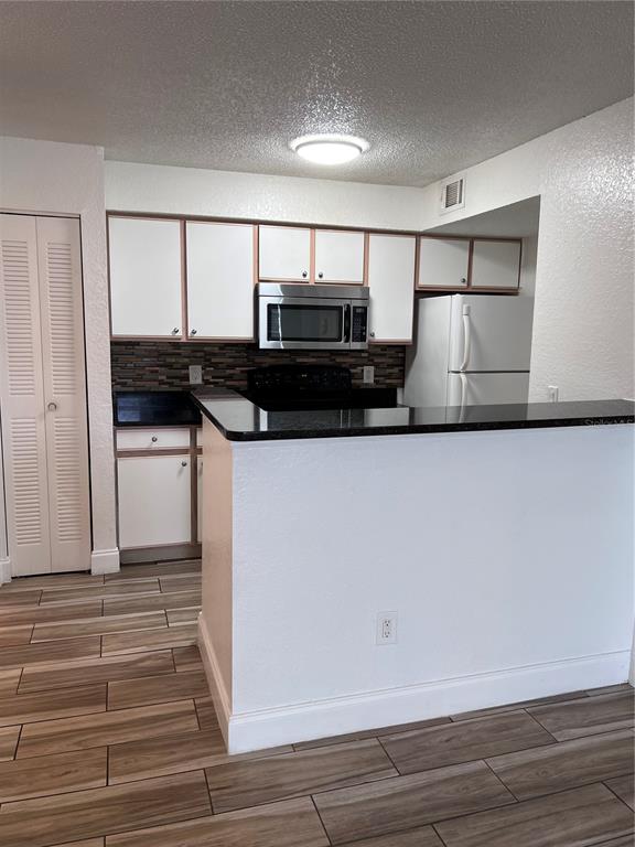 A kitchen features white cabinets, black countertops, a tiled backsplash, and wood-look tile flooring — 2208 ANTIGUA PLACE UNIT 938, KISSIMMEE, FL