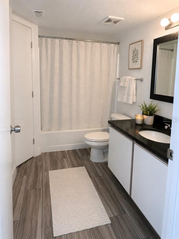 A bathroom features a white vanity with a black countertop, a shower-tub combo, and wood-look flooring — 2208 ANTIGUA PLACE UNIT 938, KISSIMMEE, FL