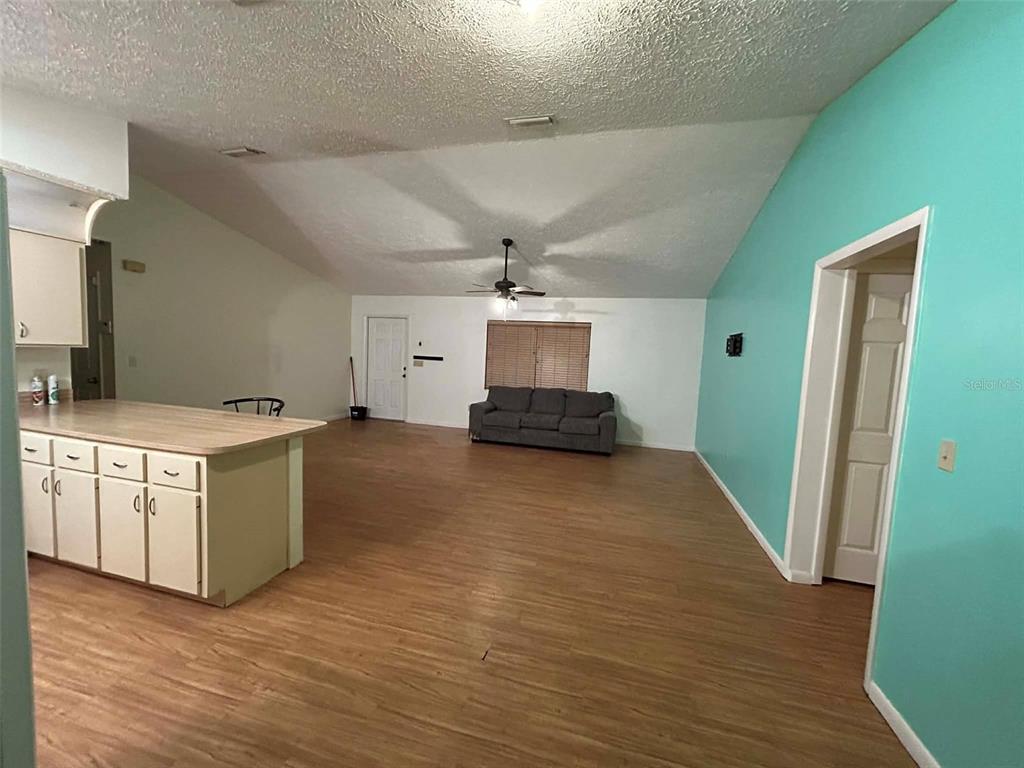 An open-concept living area features light wood-look flooring, a kitchen island, and a teal wall — 3137 CARLTON AVENUE, LAKE PLACID, FL