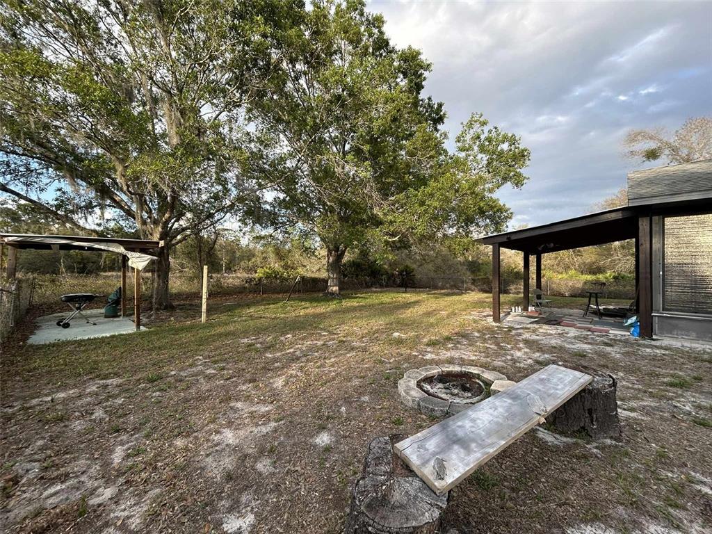 A backyard features a fire pit, a wooden bench, and two covered patio areas — 3137 CARLTON AVENUE, LAKE PLACID, FL