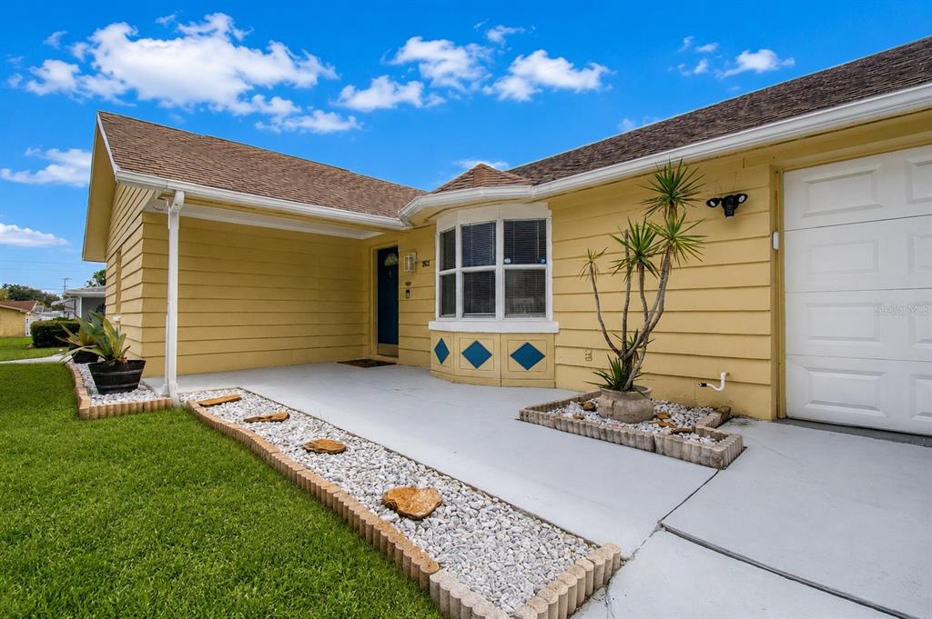 A yellow house exterior features a bay window, a covered porch, and landscaped rock beds — 3652 WESTCHESTER DRIVE, HOLIDAY, FL