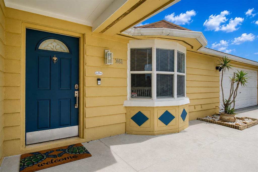 A yellow house exterior features a blue front door, a bay window, and a welcome mat — 3652 WESTCHESTER DRIVE, HOLIDAY, FL
