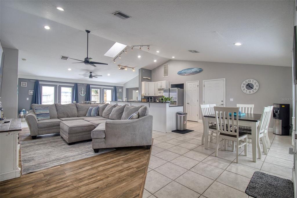 An open-concept living and dining area features a large sectional sofa, tile flooring, and vaulted ceilings — 3652 WESTCHESTER DRIVE, HOLIDAY, FL