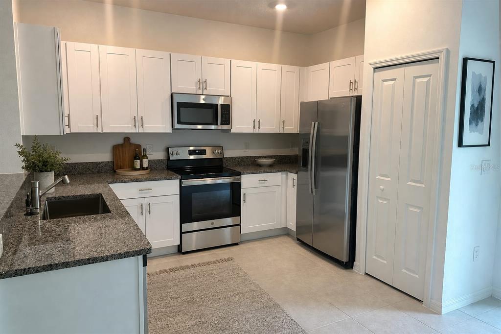 A kitchen features white cabinets, granite countertops, stainless steel appliances, and a tile floor — 17649 NECTAR FLUME DRIVE, LAND O LAKES, FL