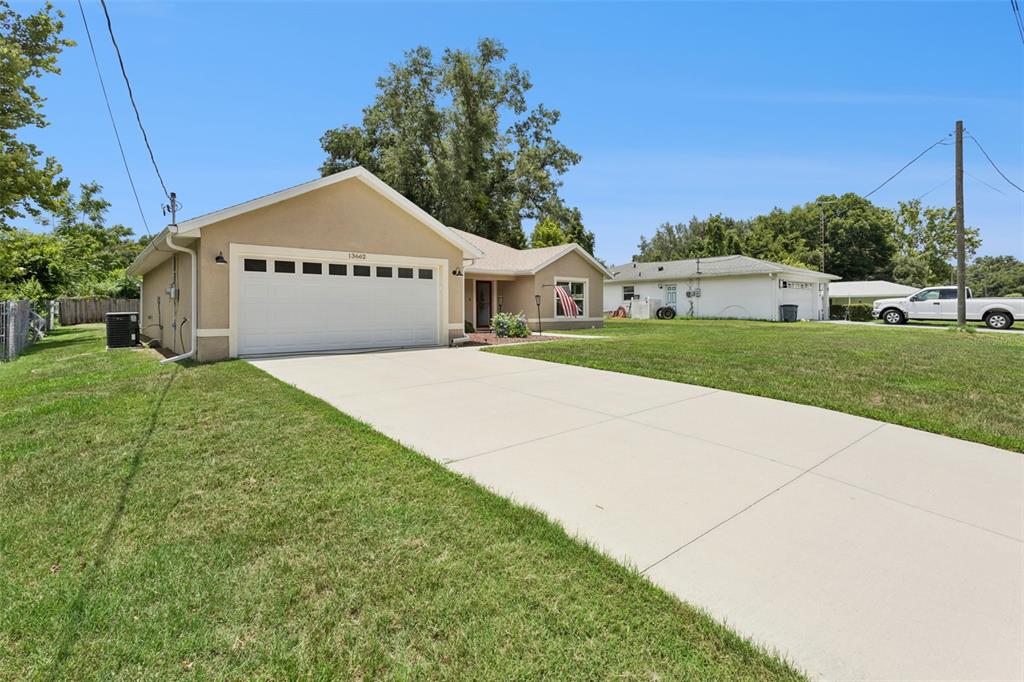 A tan single-story house with a white garage door and a concrete driveway — 13662 SE 55TH AVENUE, SUMMERFIELD, FL