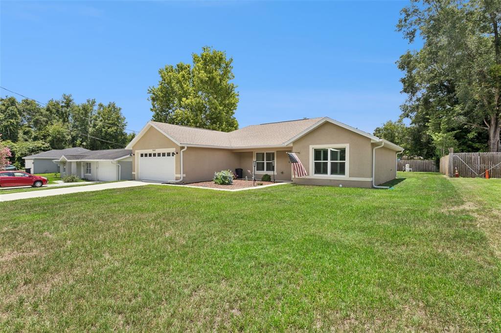A tan single-story house with a white garage and a large front lawn — 13662 SE 55TH AVENUE, SUMMERFIELD, FL
