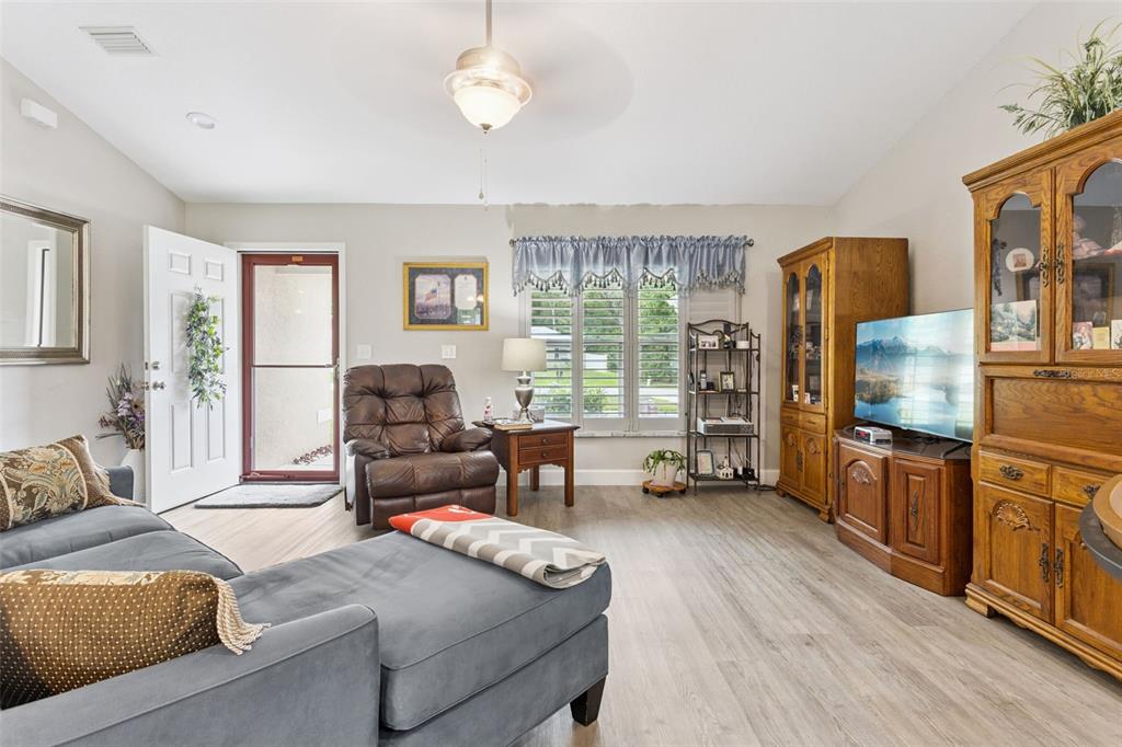 A living room features light wood-look flooring, a gray sectional sofa, and a wooden entertainment center — 13662 SE 55TH AVENUE, SUMMERFIELD, FL