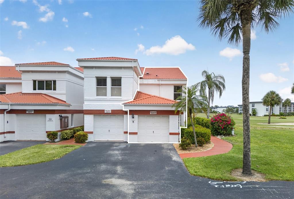 A two-story townhouse with a white stucco exterior, red tile roof, and two garage doors — 1990 LEISURE DRIVE UNIT 3, FORT MYERS, FL