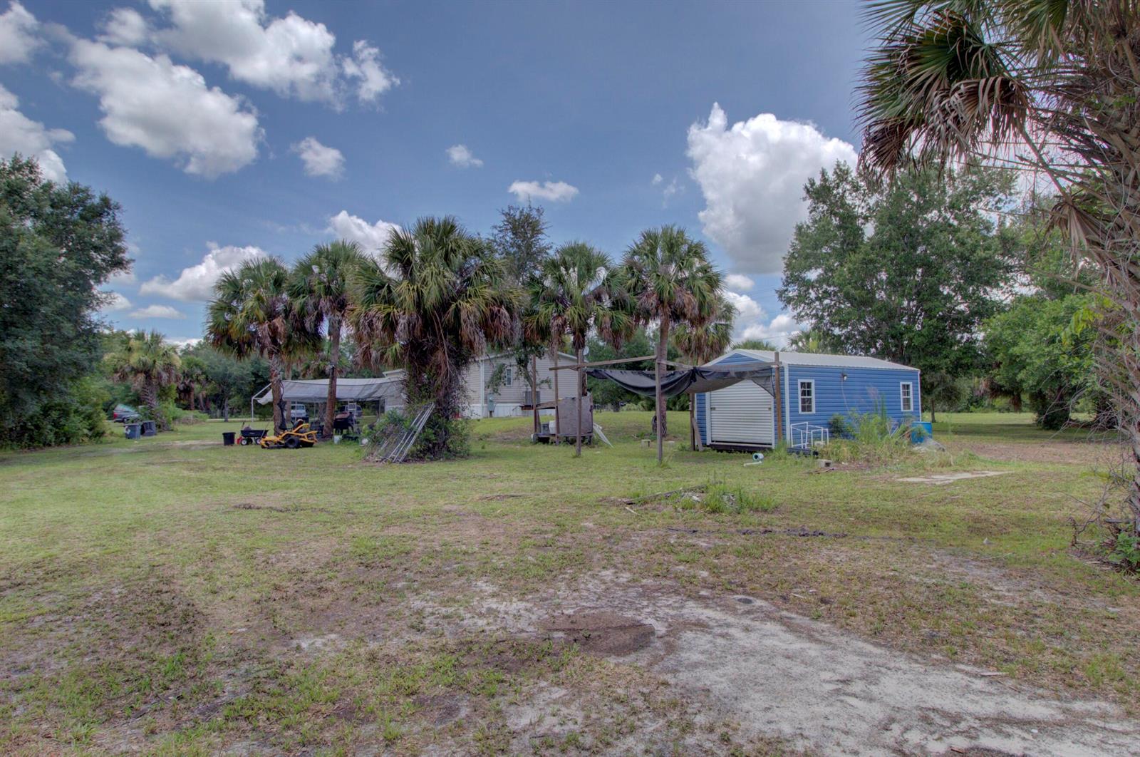 A grassy yard features a blue shed, palm trees, and a covered outdoor area — 19212 NW 280th Street, Okeechobee FL 34972, OKEECHOBEE, FL