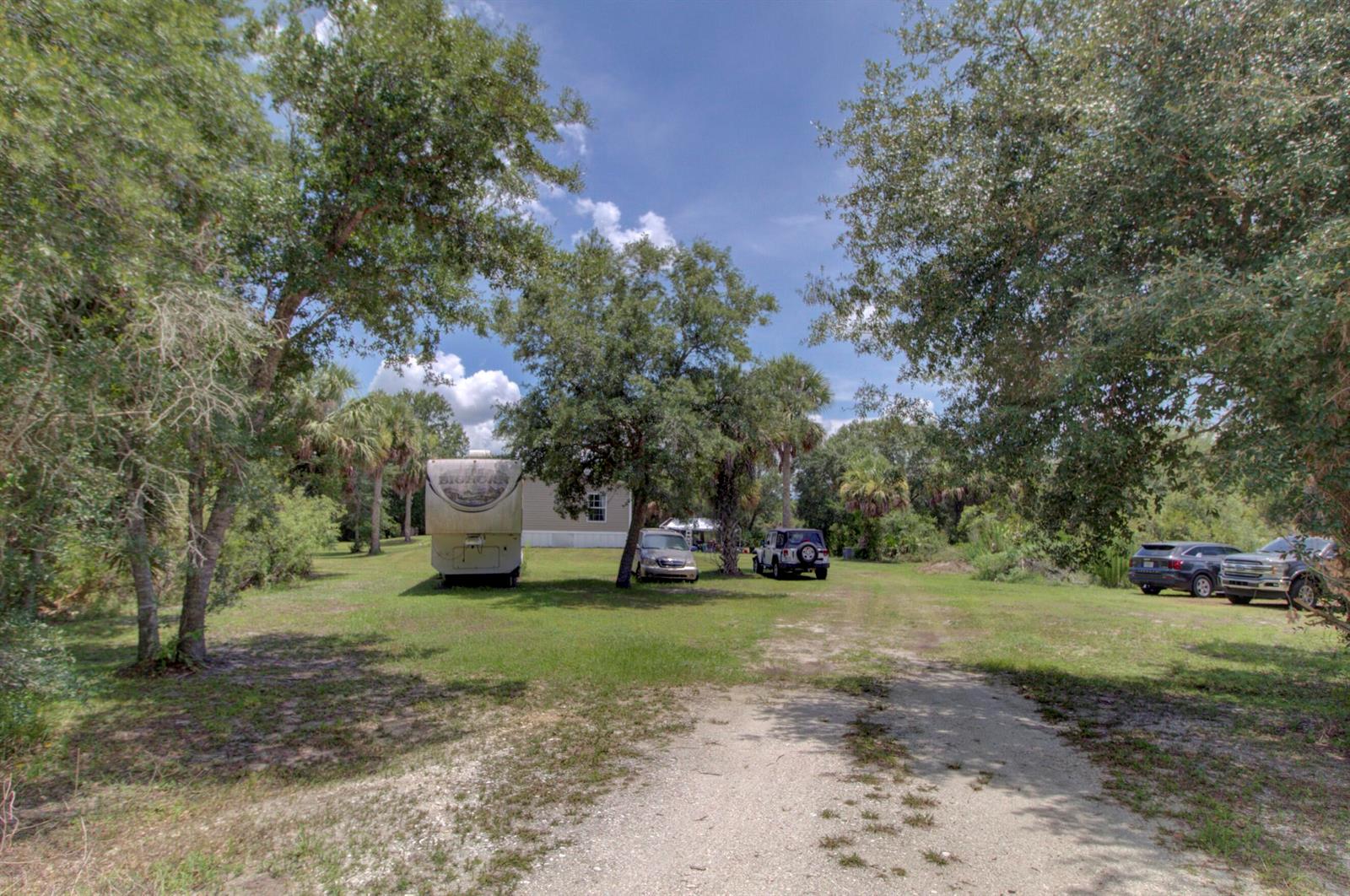 A gravel driveway leads to a grassy yard with a camper, vehicles, and mature trees — 19212 NW 280th Street, Okeechobee FL 34972, OKEECHOBEE, FL