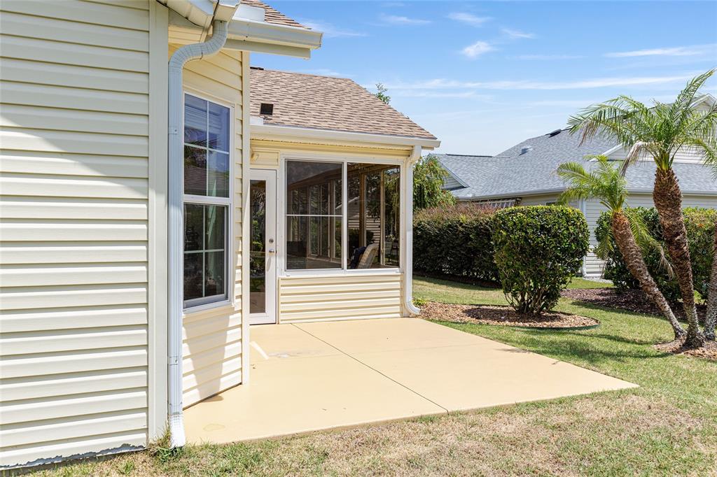 A concrete patio sits outside a house with beige siding and a screened-in porch — 2047 DUNSTER COURT, THE VILLAGES, FL