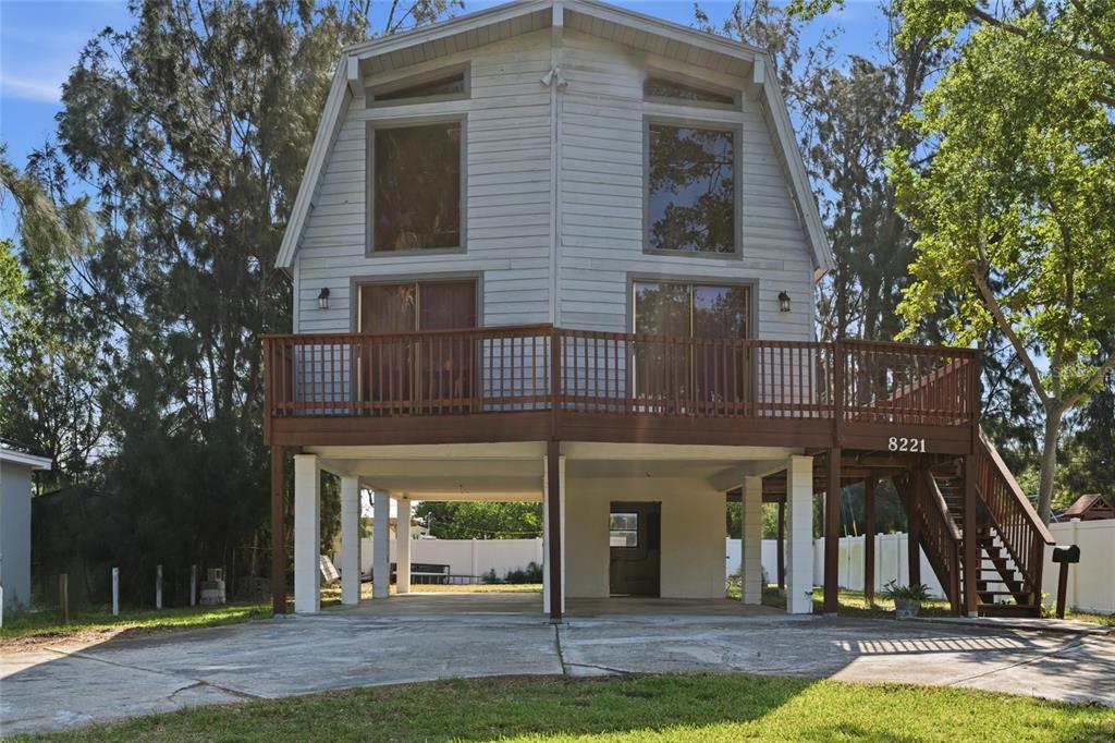 A two-story house with a gambrel roof is elevated on concrete pillars above a driveway — 8221 RIVERSIDE DR NE, ST PETERSBURG, FL