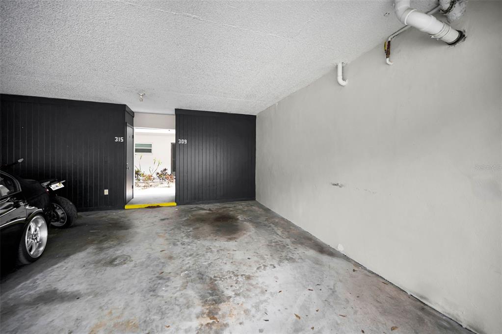 A covered parking space features a concrete floor, a plain wall, and two unit doors — 1127 KING ARTHUR COURT UNIT 309, DUNEDIN, FL