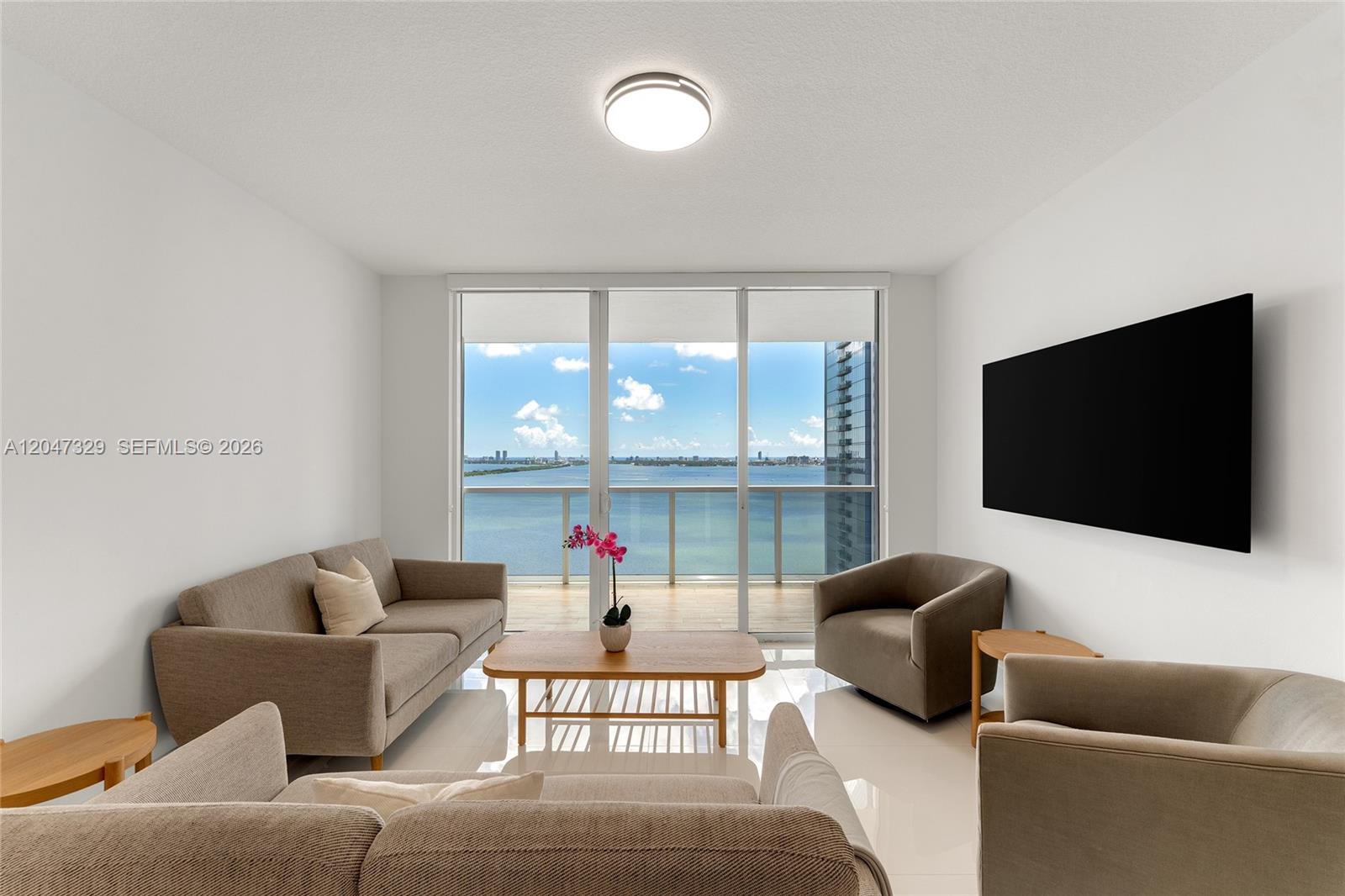 A living room features neutral furniture, white tile floors, and a balcony overlooking the water — 600 NE 27th St # 2904, Miami FL 33137, MIAMI, FL