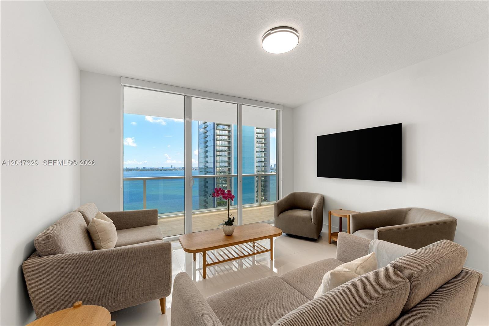 A living room features beige furniture, a wooden coffee table, and floor-to-ceiling windows overlooking water — 600 NE 27th St # 2904, Miami FL 33137, MIAMI, FL