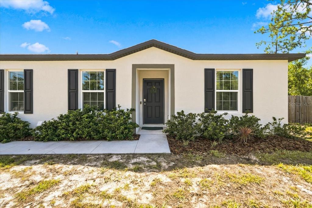 The exterior of a single-story house features a dark front door, shutters, and landscaping — 15186 DUCK HAWK ROAD, WEEKI WACHEE, FL