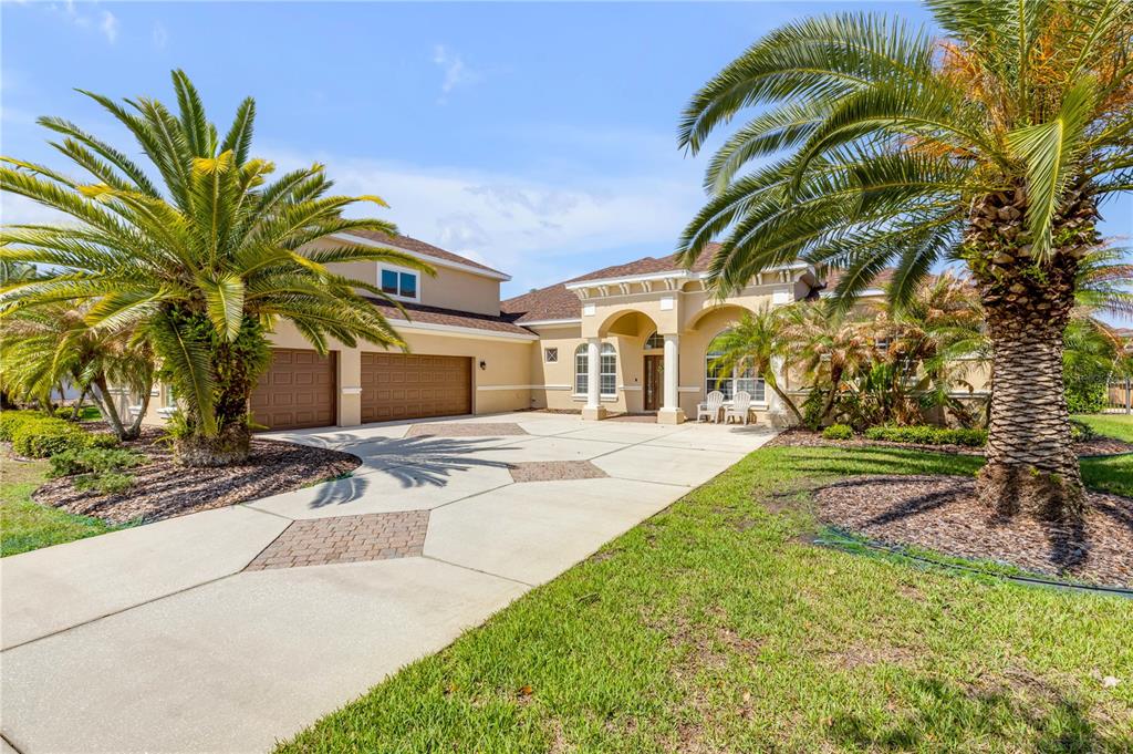 A tan house with a multi-car garage, arched entryway, and palm trees in the front yard — 3377 CATERINA DRIVE, NEW SMYRNA BEACH, FL