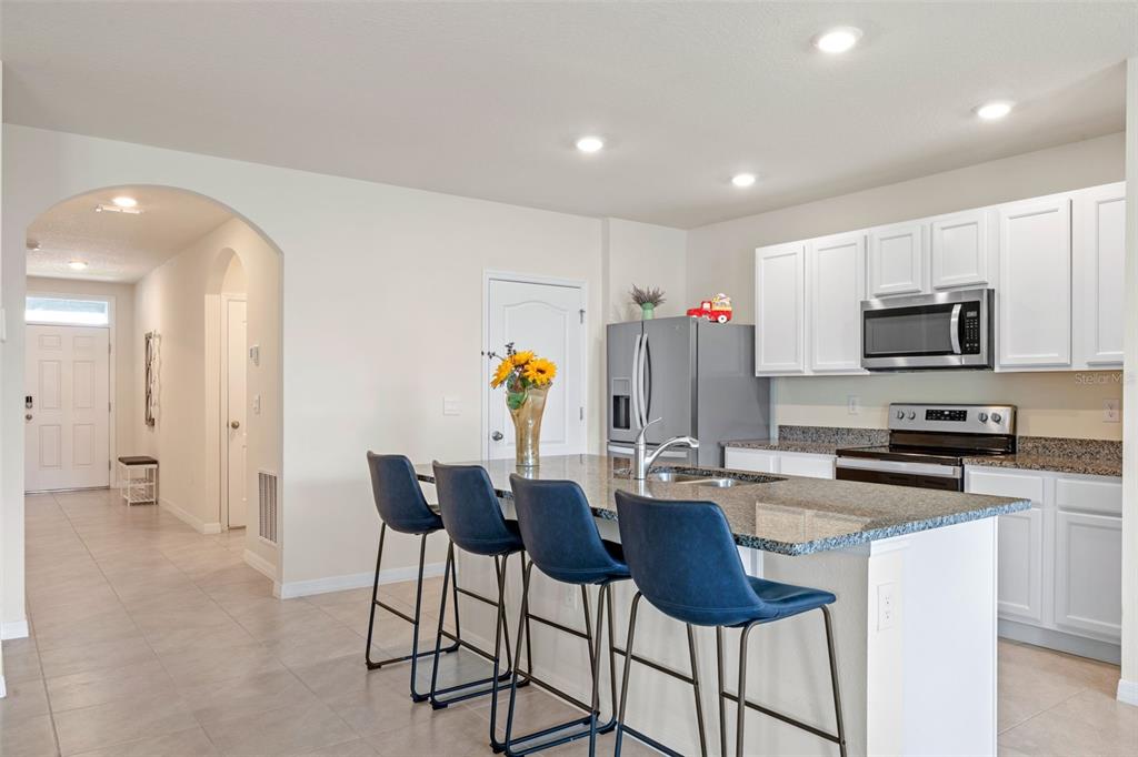A kitchen features a granite-topped island with blue bar stools and white cabinetry — 5362 DOUGLAS FIR DRIVE, ST CLOUD, FL