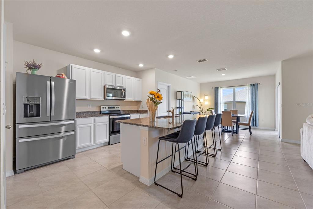 A kitchen features white cabinets, granite countertops, stainless steel appliances, and a central island — 5362 DOUGLAS FIR DRIVE, ST CLOUD, FL